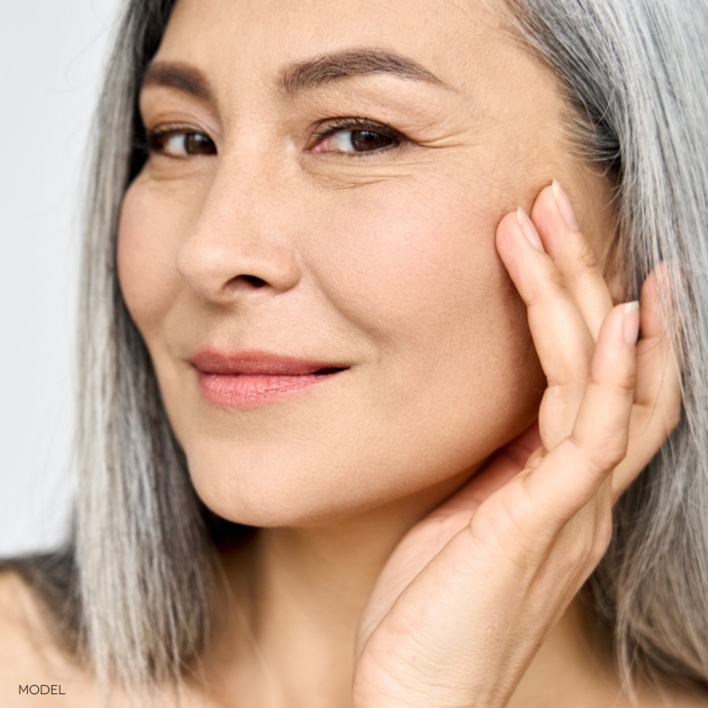 middle aged woman with grey hair, smiling with hand up to face